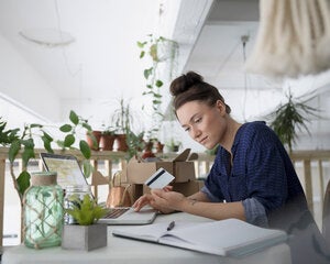 Female small business owner looking over finances and holding a credit card.