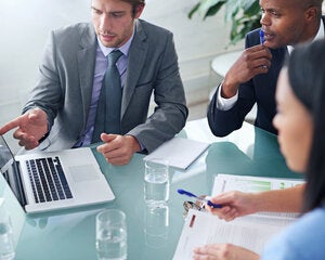 three business professionals in suits looking at a laptop screen