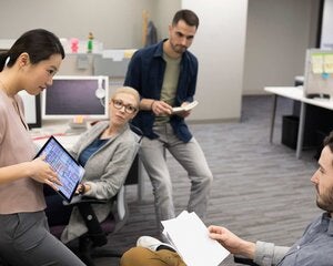 Businesswoman with digital tablet leading meeting at office cubicle