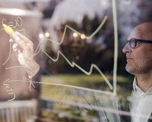 man with glasses writing a calculation on glass