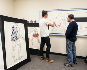 A student and an art teacher looking at sketches on a whiteboard