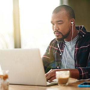 man wearng earbuds looking at a laptop