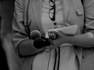 Woman holding microphones and recorder, writing on note pad