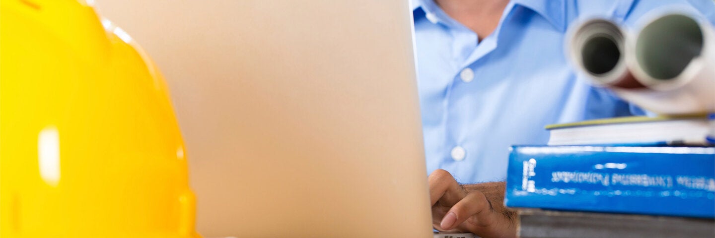 Construction manager in office typing on laptop.