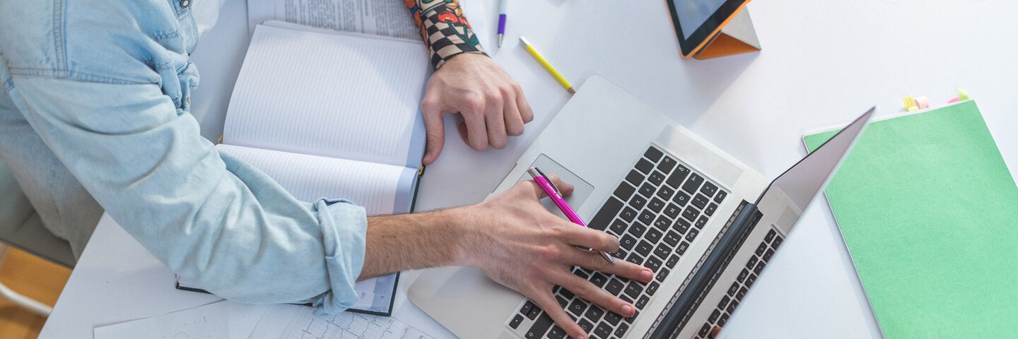 a view from above of a person on their laptop and an open note book