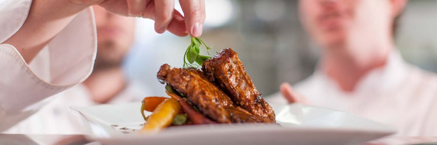 close up view of a chef adding a garnish to a dinner plate