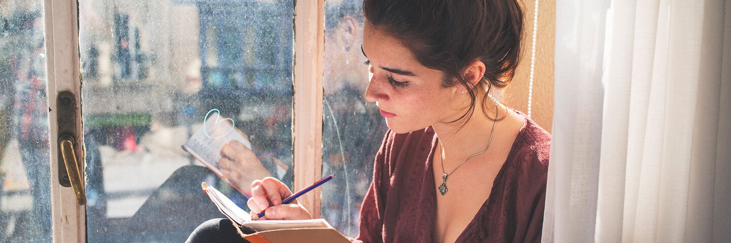 Young woman writing in notebook sitting in window