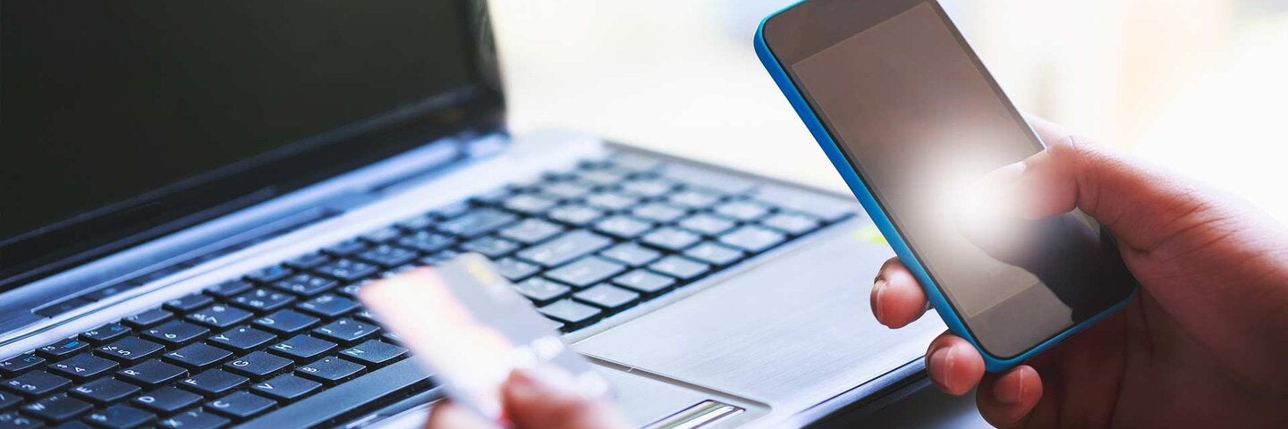 man holding smartphone and credit card in front of laptop