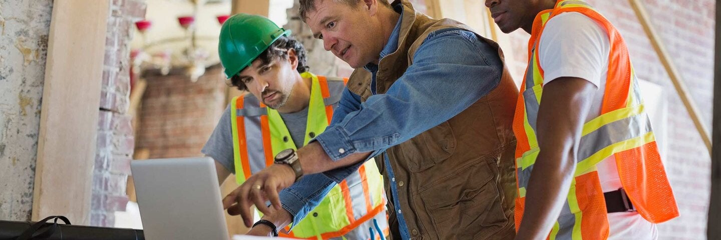 Foreman discussing plan on laptop with tradesmen at construction site