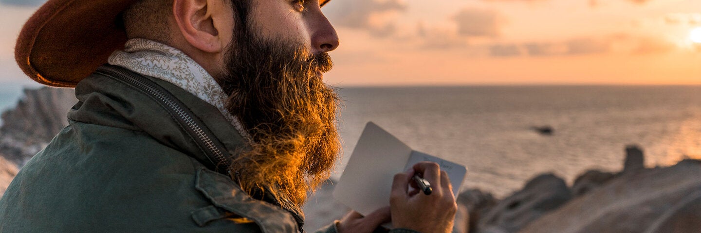 Man with a hat writing at the sea
