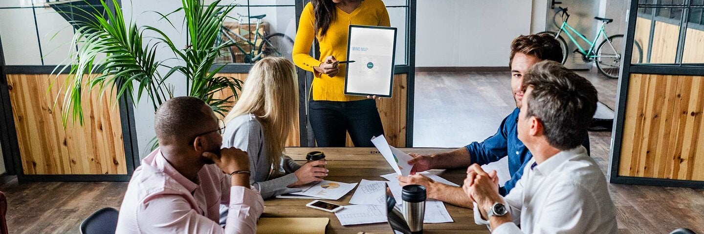 business woman presenting in front of a table of other professionals
