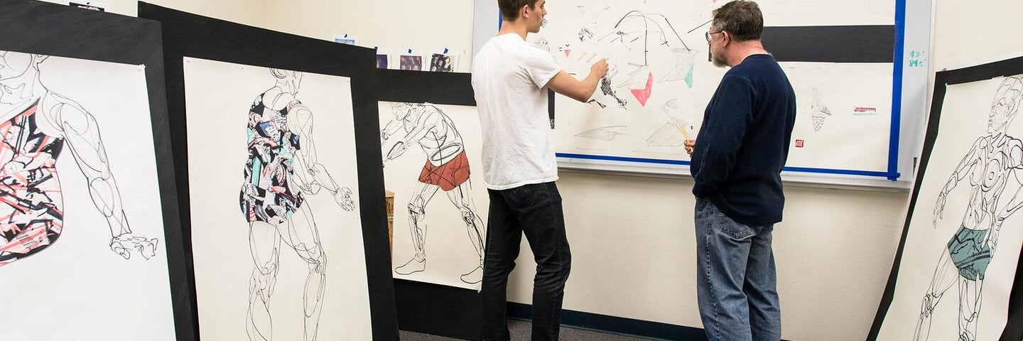 A student and an art teacher looking at sketches on a whiteboard
