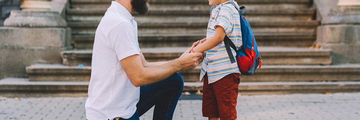a dad kneeling down to talk eye to eye with his young son
