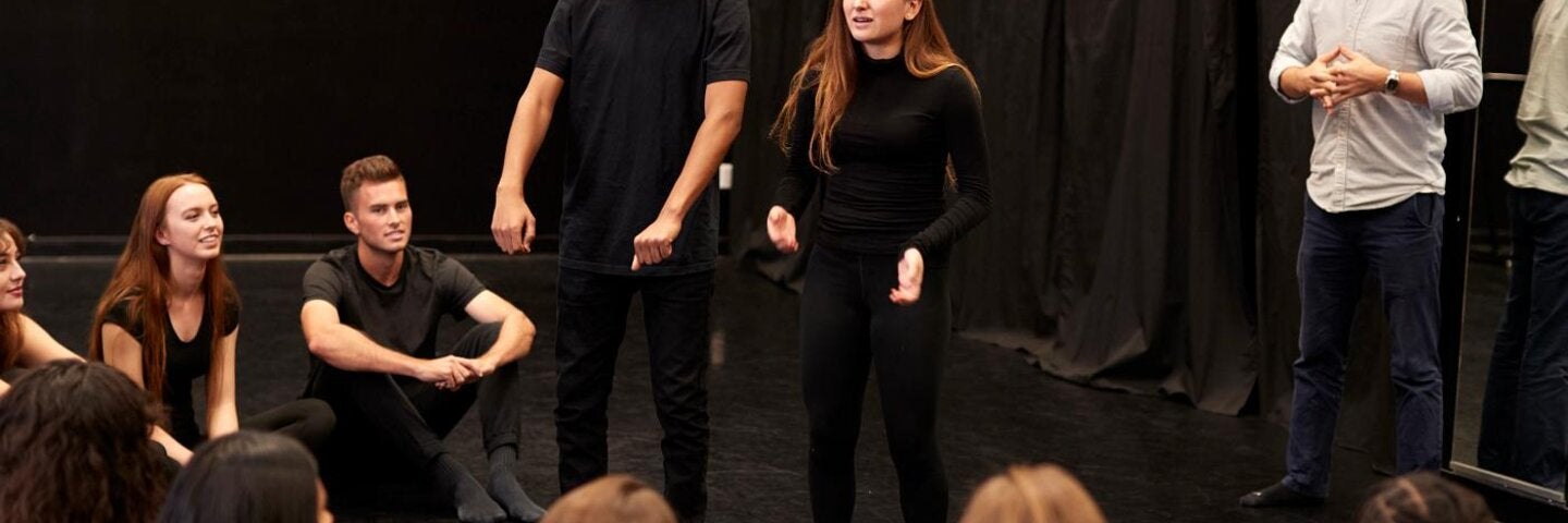 Teacher With Male And Female Drama Students At Performing Arts School In Studio Improvisation Class